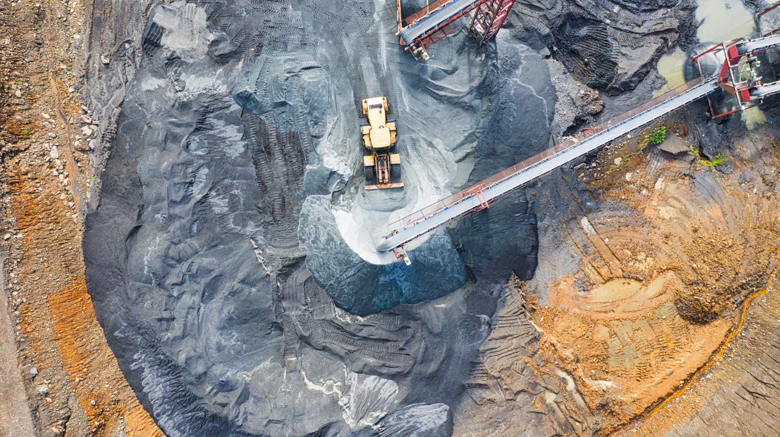Aerial view of a mining site with heavy equipment and conveyor belts moving extracted material.