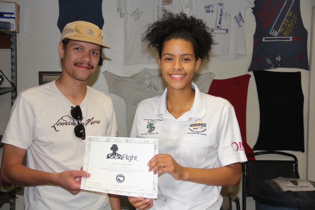 Two aviation students smiling and holding a certificate that reads "solo flight"