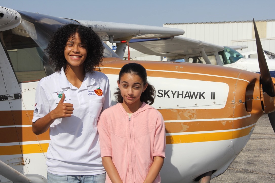 Two aviation students smiling in front of a propeller plane.
