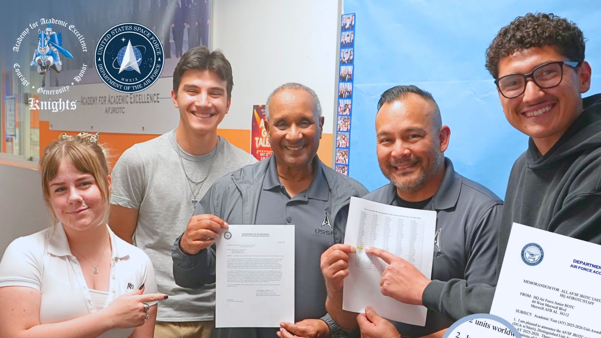 AAE Five students and instructors from an Air Force JROTC program smile and hold documents while posing inside a classroom, with Academy for Academic Excellence and U.S. Space Force signage displayed in the background.