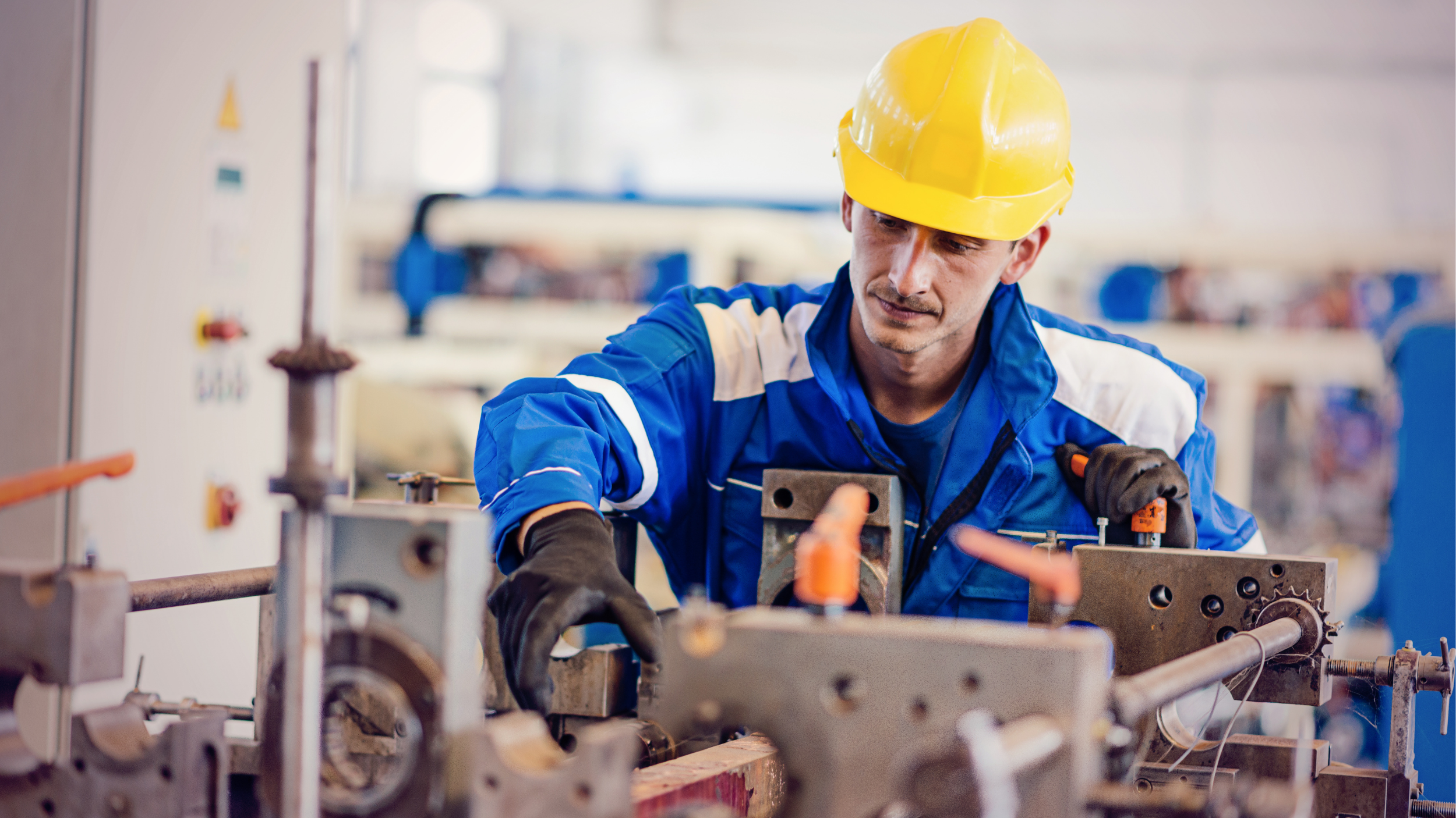 Lowe’s Worker in a yellow hard hat and blue uniform operates industrial machinery in a manufacturing facility.