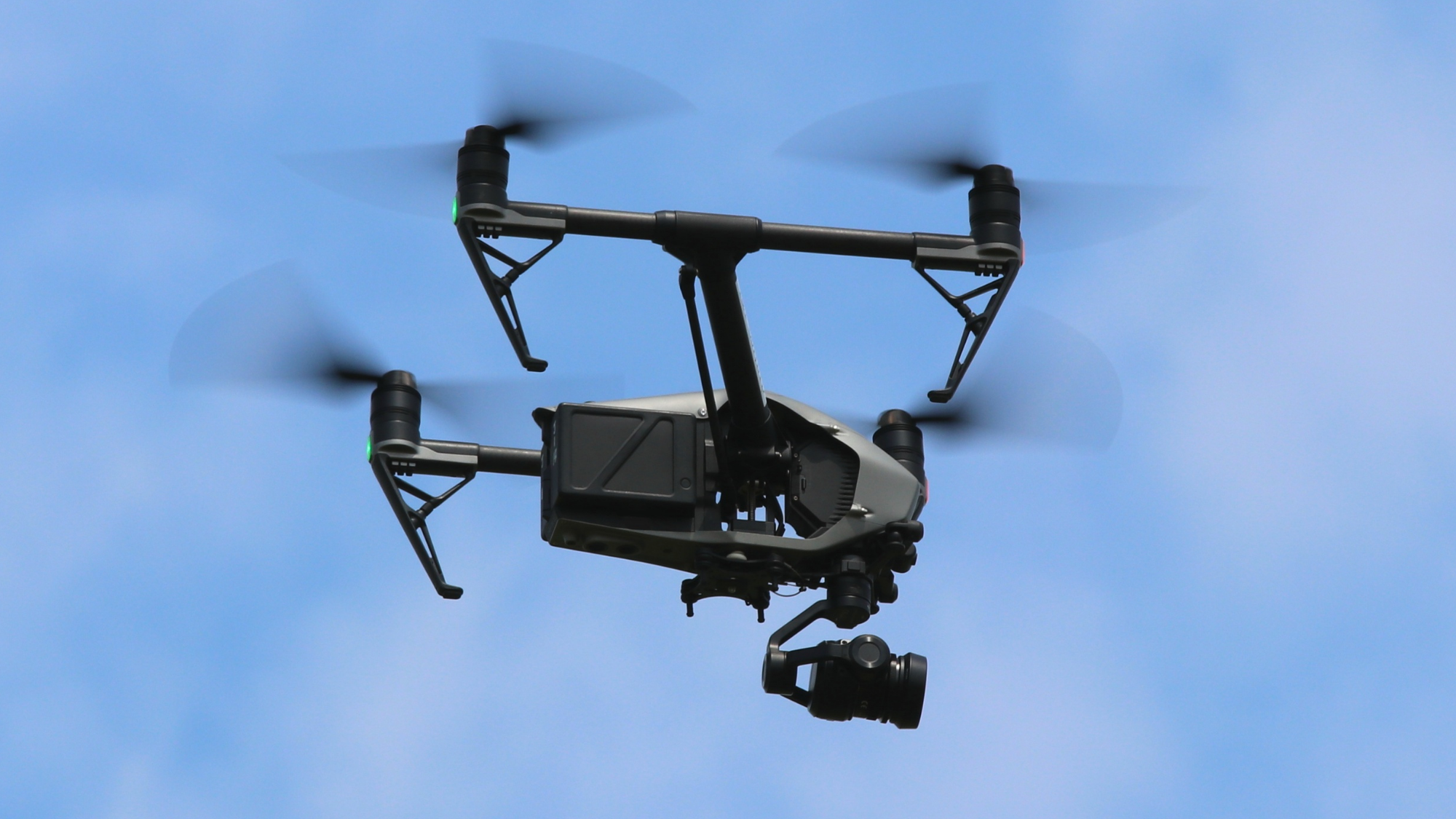 PoliceDrone Quadcopter drone with camera hovering in the sky, propellers in motion against a clear blue background.