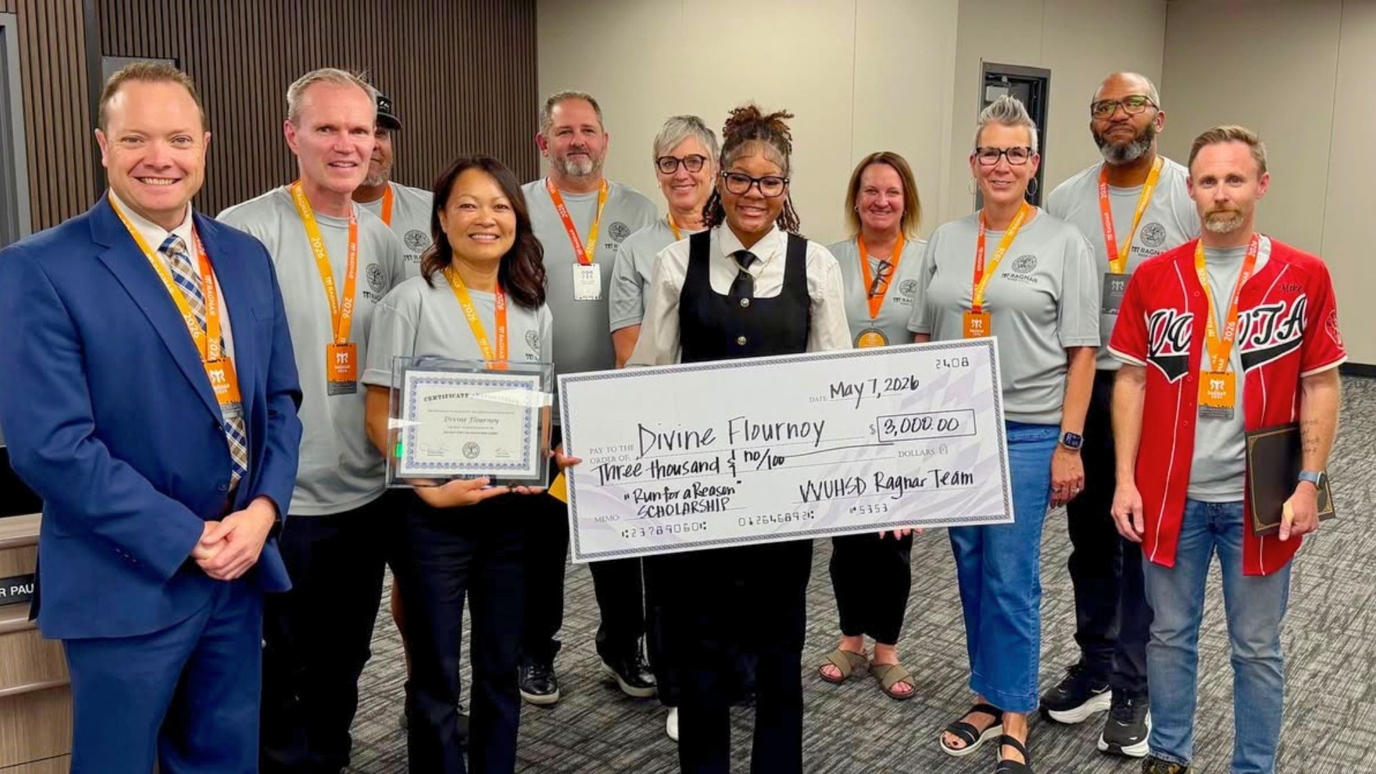 Group of community members and organizers posing indoors during a scholarship presentation, with one student holding a large $3,000 scholarship check and certificate surrounded by supporters and event participants.