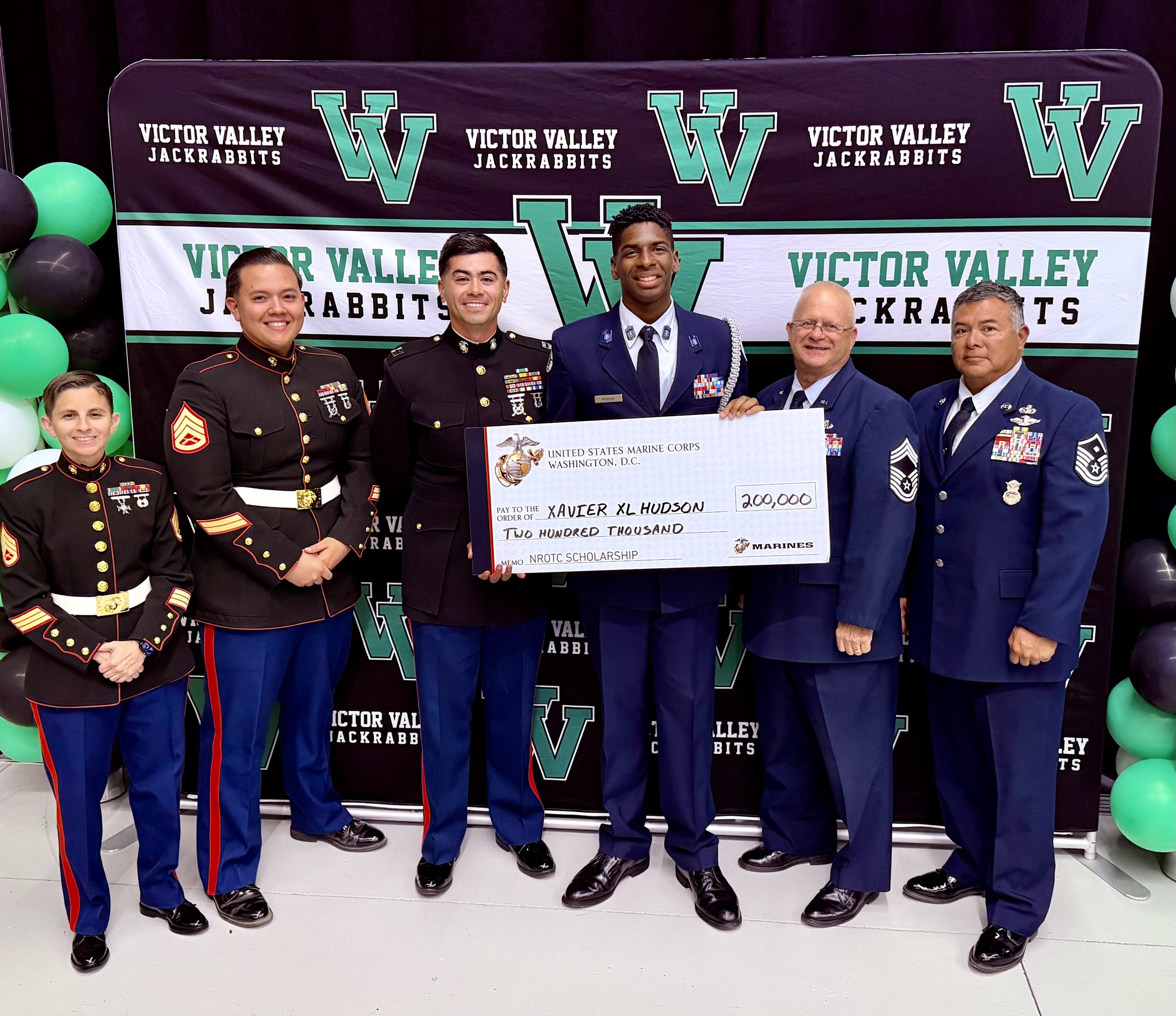 ScholarshipAward Group of uniformed service members and officials stand in front of a Victor Valley Jackrabbits backdrop, presenting a $200,000 NROTC scholarship check to a student.
