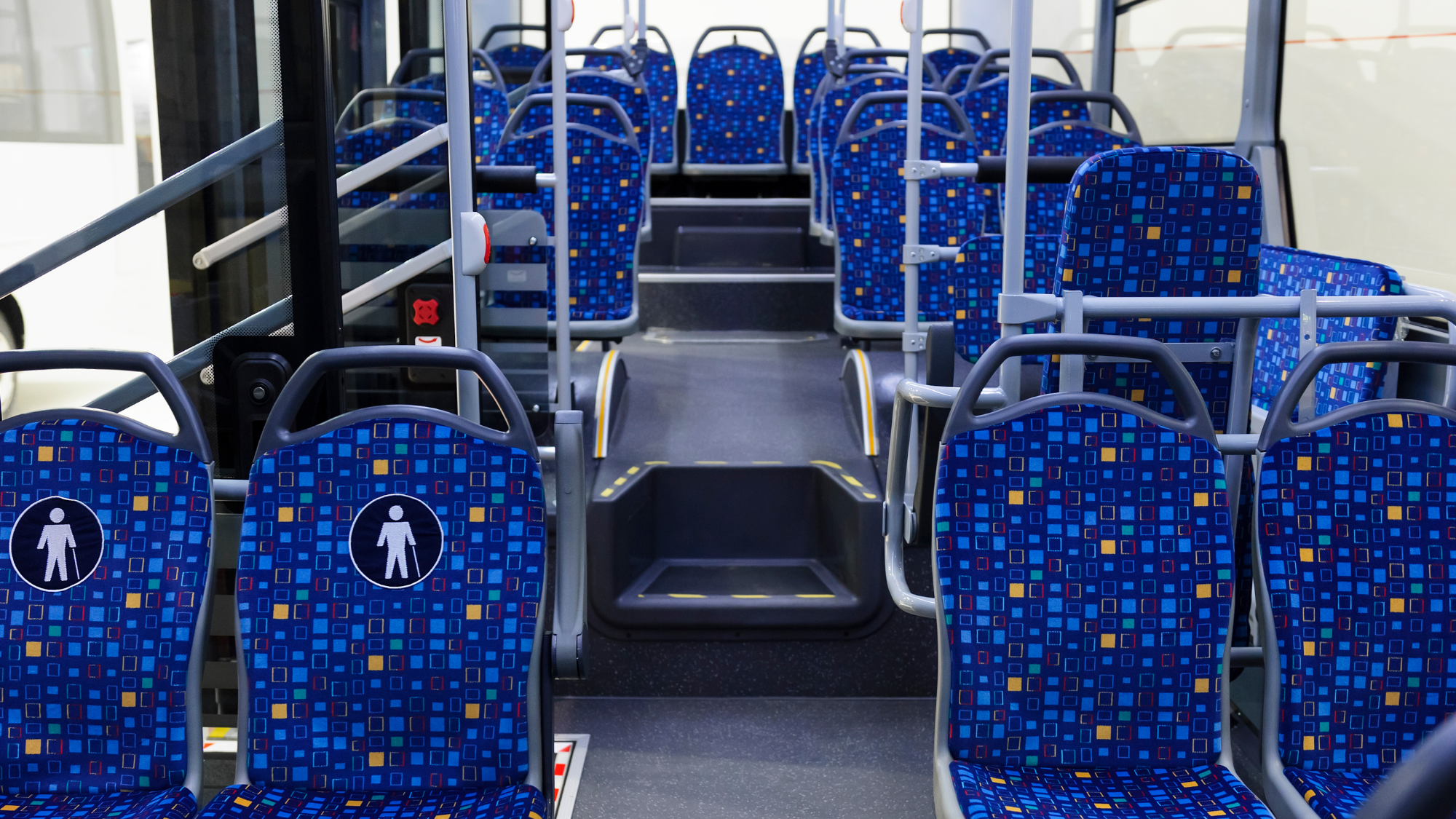 bustour Interior of a modern public transit bus with rows of blue patterned seats, handrails, and a center aisle leading toward the back seating area.