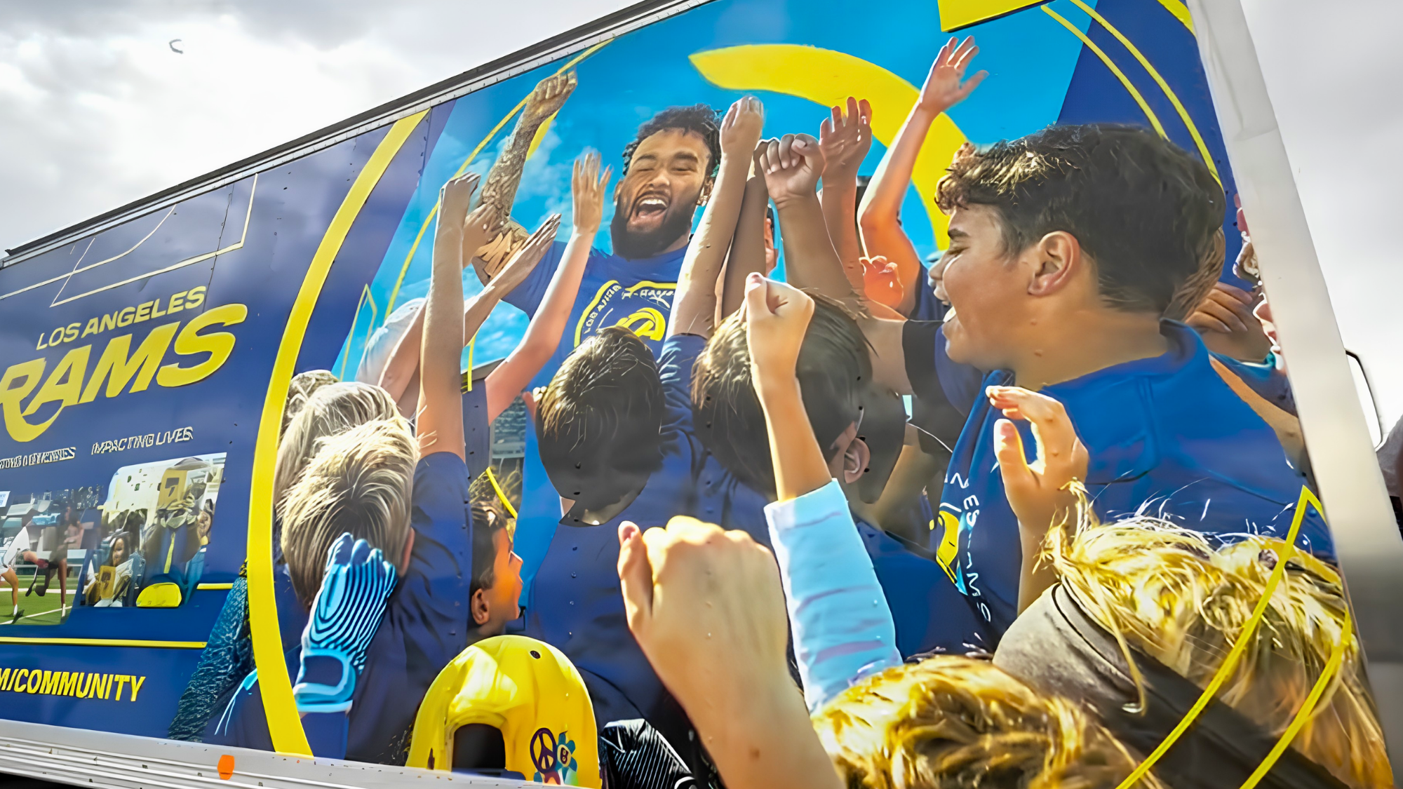 A Los Angeles Rams community outreach truck featuring a large mural of a Rams player celebrating with young fans.