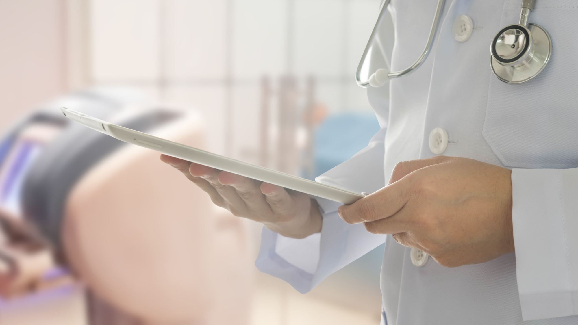 Medical A healthcare professional wearing a white lab coat and stethoscope holds a tablet in a clinical setting.